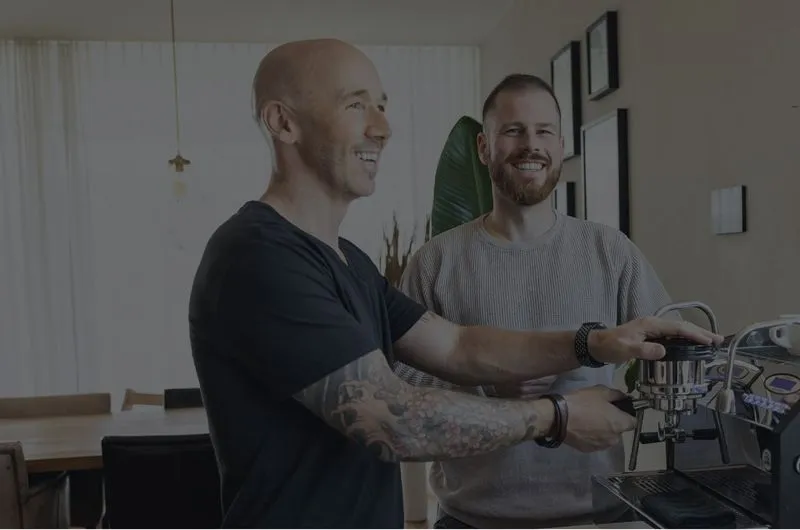 Marco und Mario stehen während einer Pause in der Nähe der Kaffeemaschine.